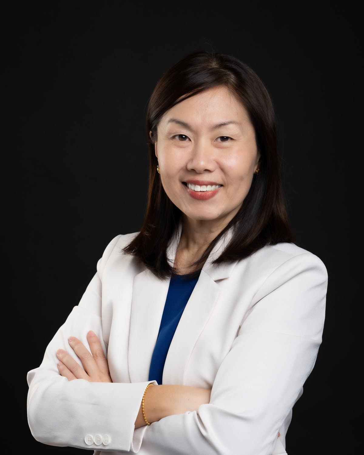 Gladys Ng smiling with her arms folded, wearing a cream blazer over a navy top