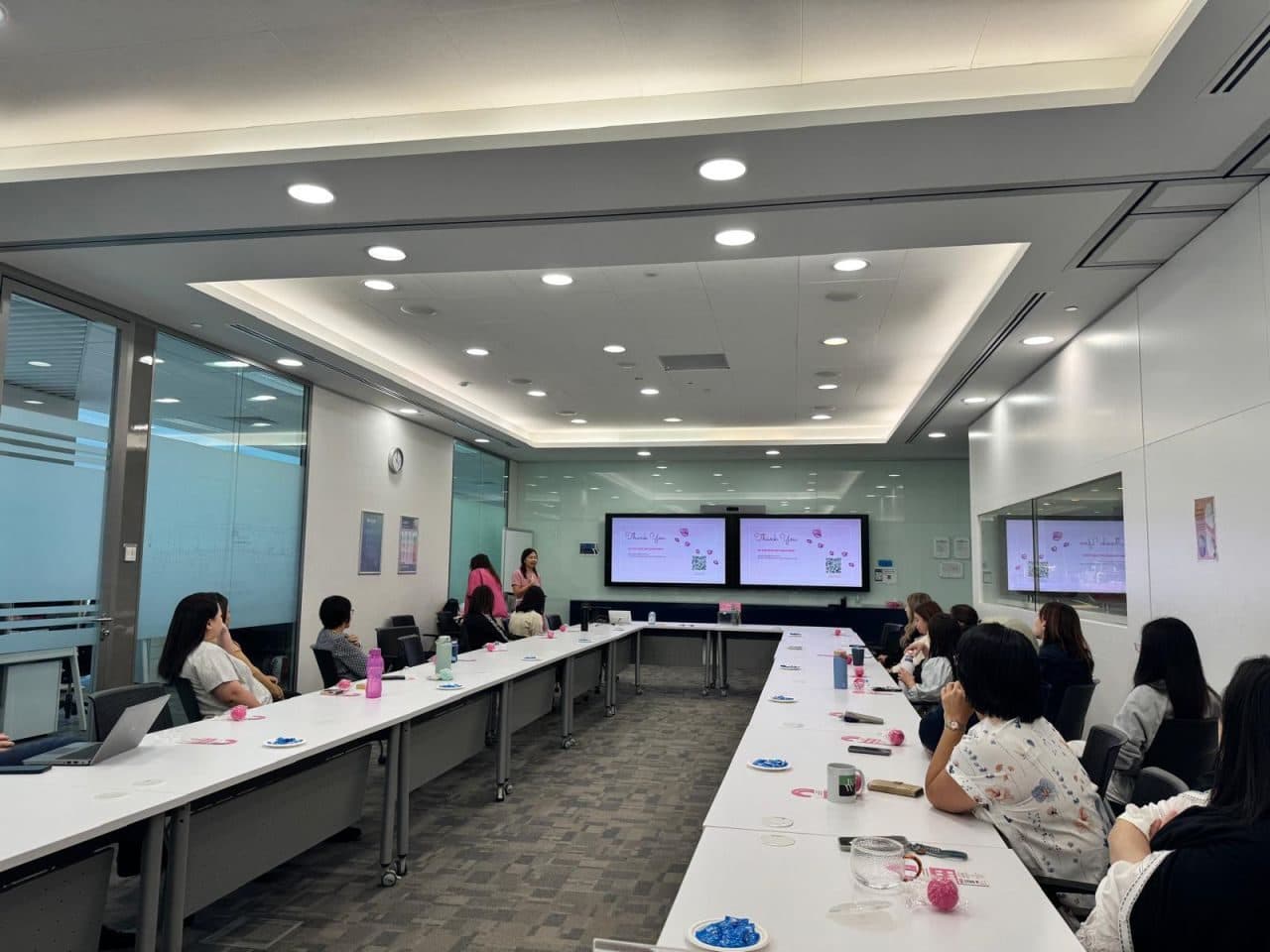 Attendees around a long table at the end of a talk, with “Thank you” slides on the screens