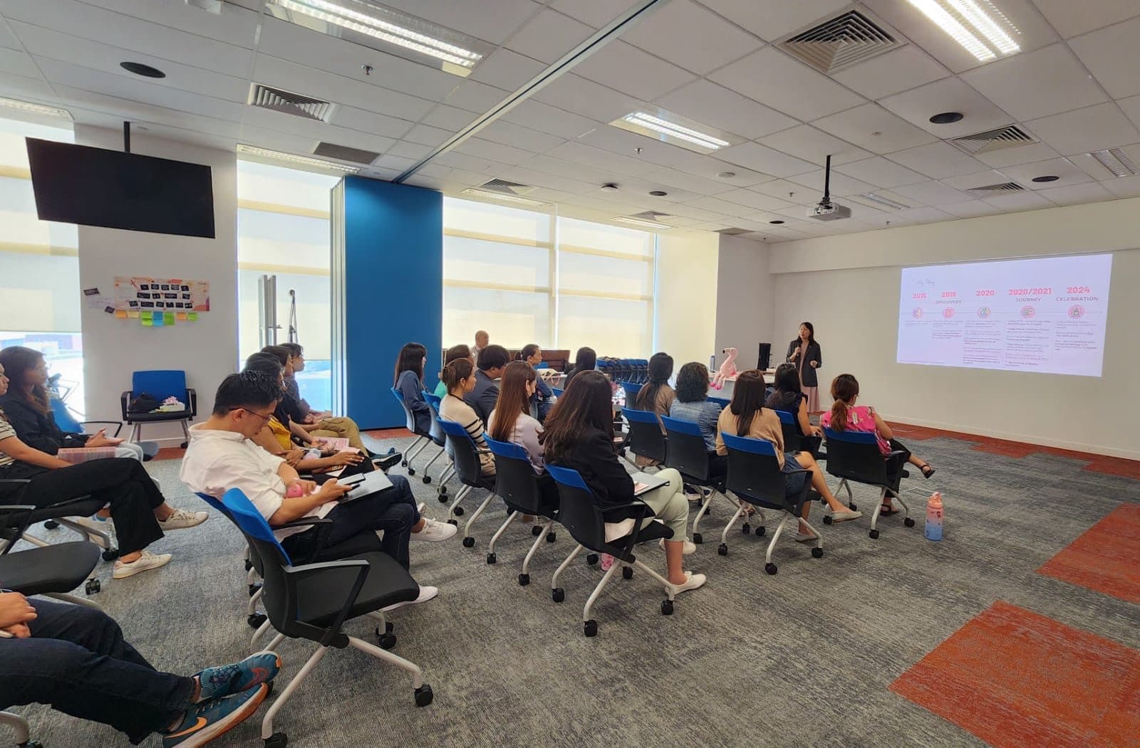 A room of around twenty colleagues listening as Gladys presents at the front